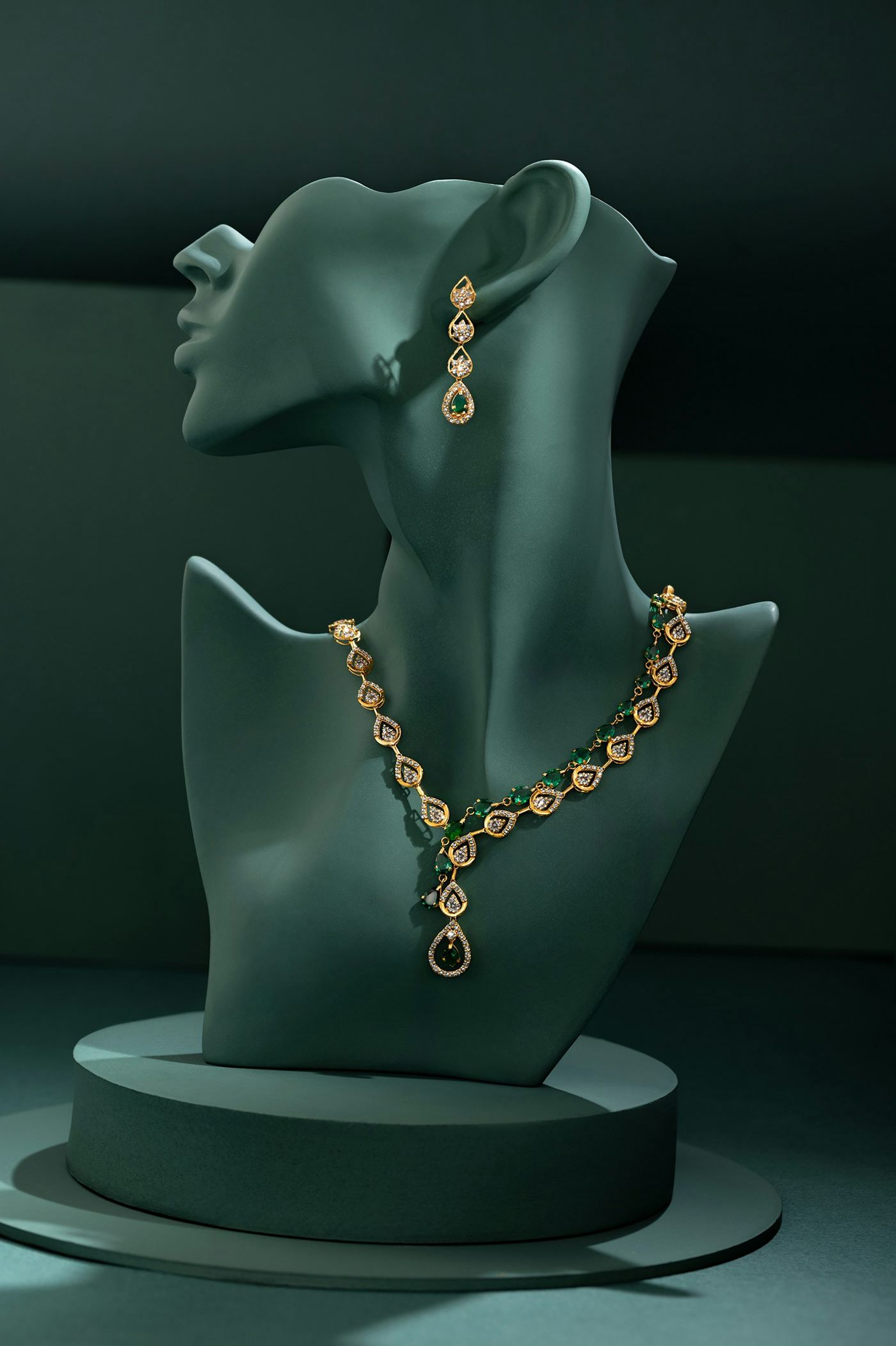 Collar y aretes de oro con esmeraldas sobre busto, fondo verde oscuro editorial