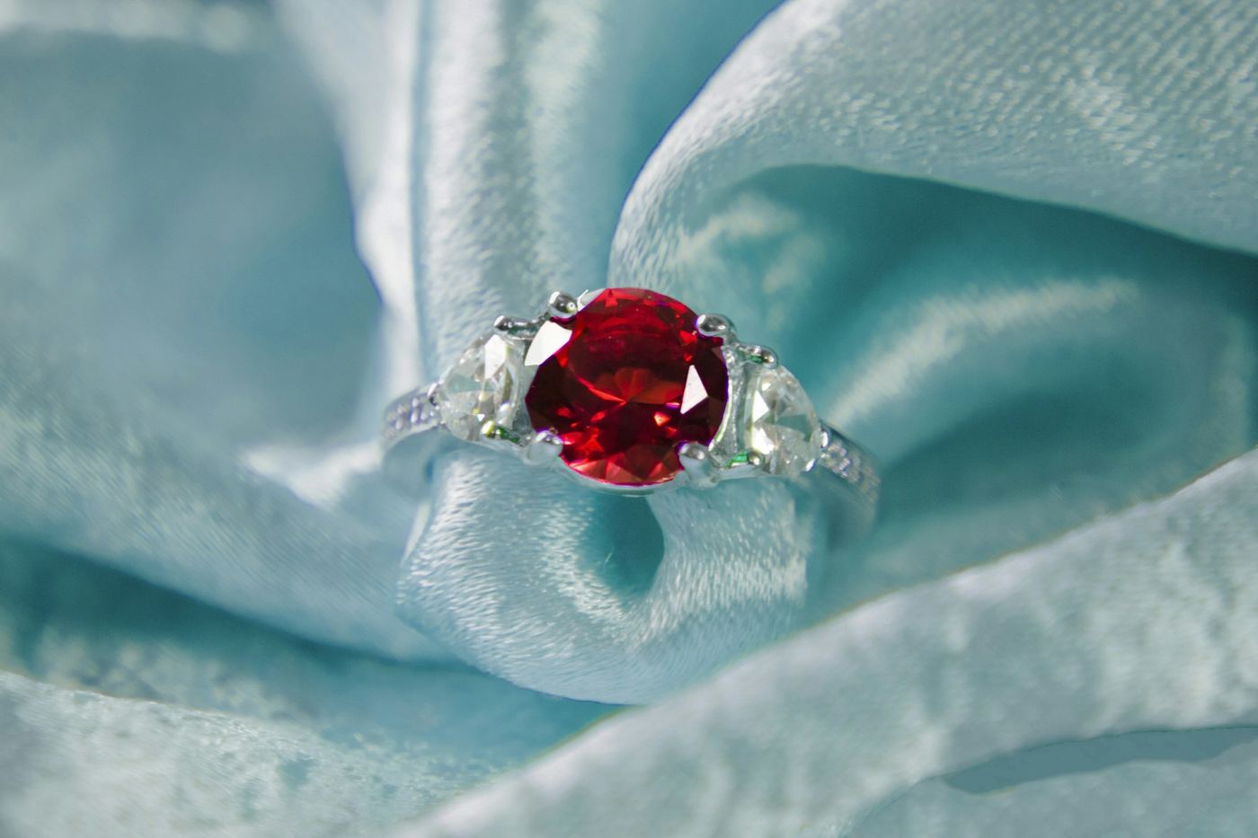 Anillo con rubí central y dos diamantes laterales sobre tela satinada verde agua